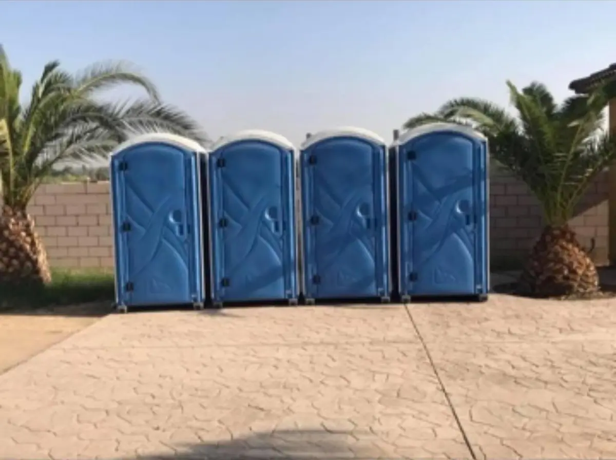 Row of four blue standard porta potties set up for an outdoor event
